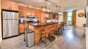 Una cocina moderna con armarios de madera, electrodomésticos de acero inoxidable y una isla central con taburetes de bar.
