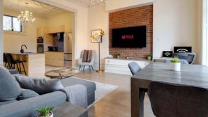 A modern living room with a fireplace, a TV mounted on the wall, a dining area, and a kitchen in the background.