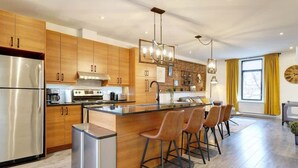 A modern kitchen with wooden cabinets, stainless steel appliances, a central island with bar stools, and a large window with curtains.