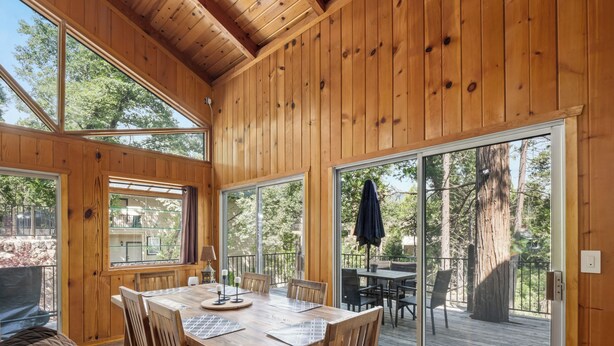 Un interior de madera con una mesa de comedor, sillas y un amplio ventanal corredero que da a una terraza exterior.