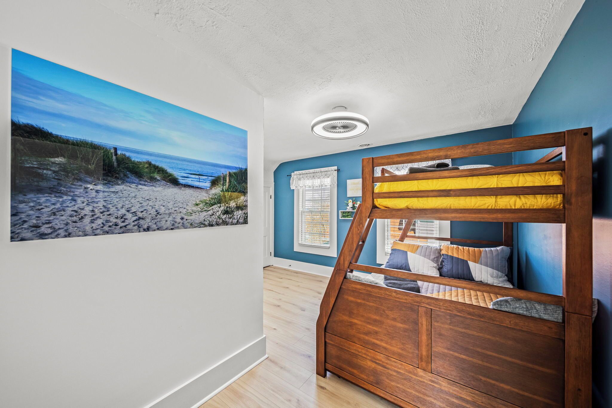 A room with a bunk bed, a beach-themed wall mural, and a ceiling fan.