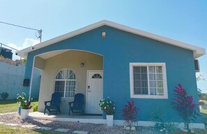 A single-story house with a blue exterior, a white door, and a small porch with two chairs.
