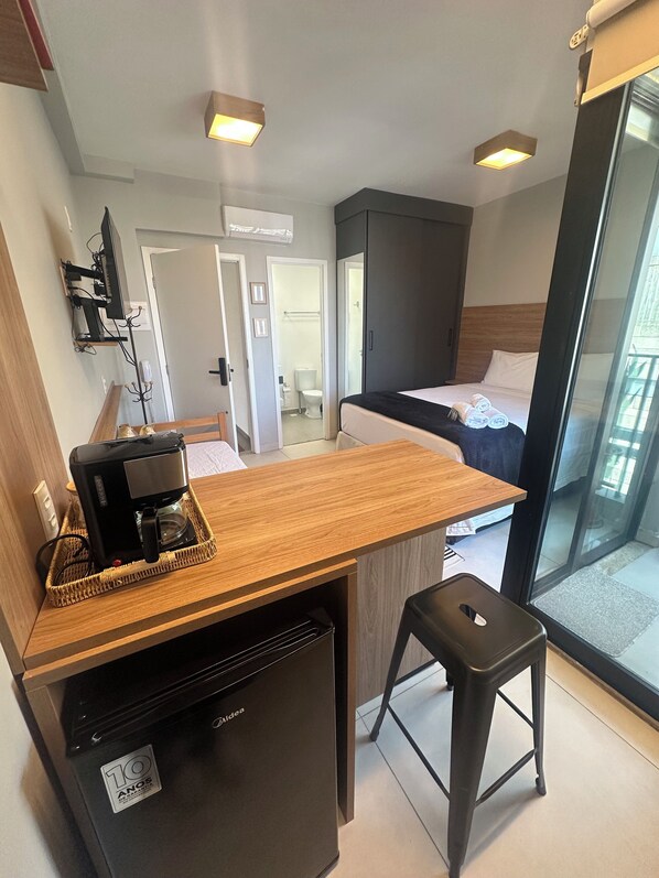 A compact hotel room with a kitchenette, a bed, and a bathroom visible through an open door.