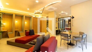 Een moderne hotel lobby met een rode bank, een eetgedeelte met een ronde tafel en stoelen, en houten lambrisering op de muren.