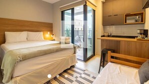 Een hotelkamer met een groot bed, een klein bureau, een kitchenette en een schuifdeur naar een balkon.