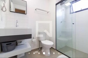 A modern bathroom with a glass shower enclosure, a white toilet, and a white sink with a towel rack above.