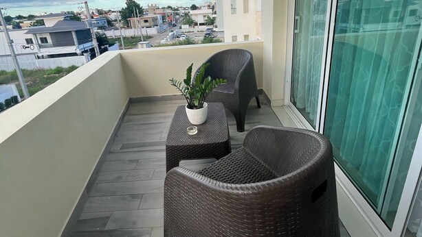 Un balcón con mobiliario de mimbre, una planta en maceta y vistas de la ciudad.