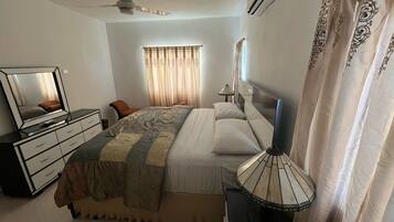 A bedroom with a bed, a dresser, a TV, a ceiling fan, and a window with curtains.