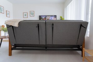 A grey sofa with a wooden frame and a television on a stand in the background.