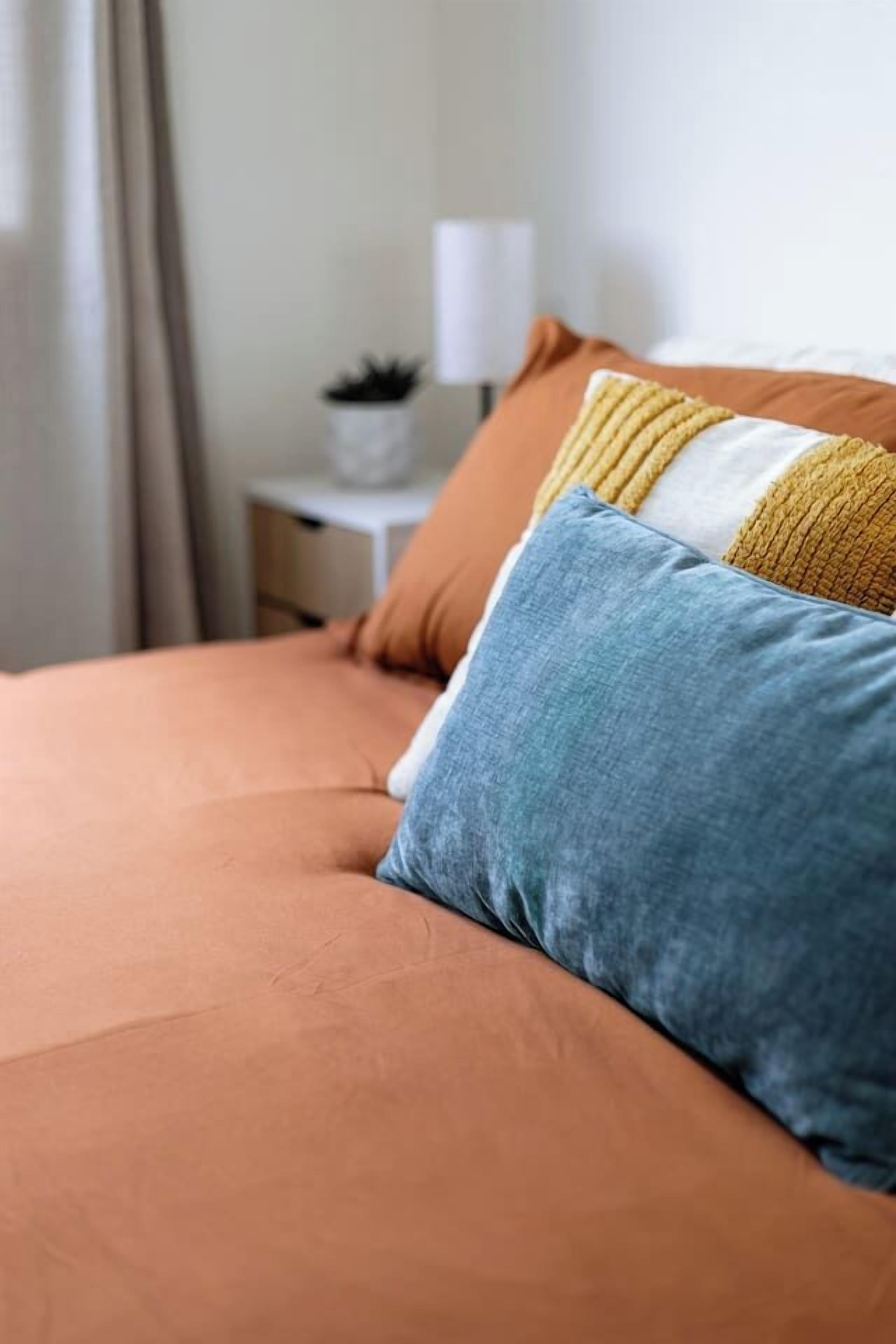 A bed with a single blue pillow and a yellow and white striped pillow.