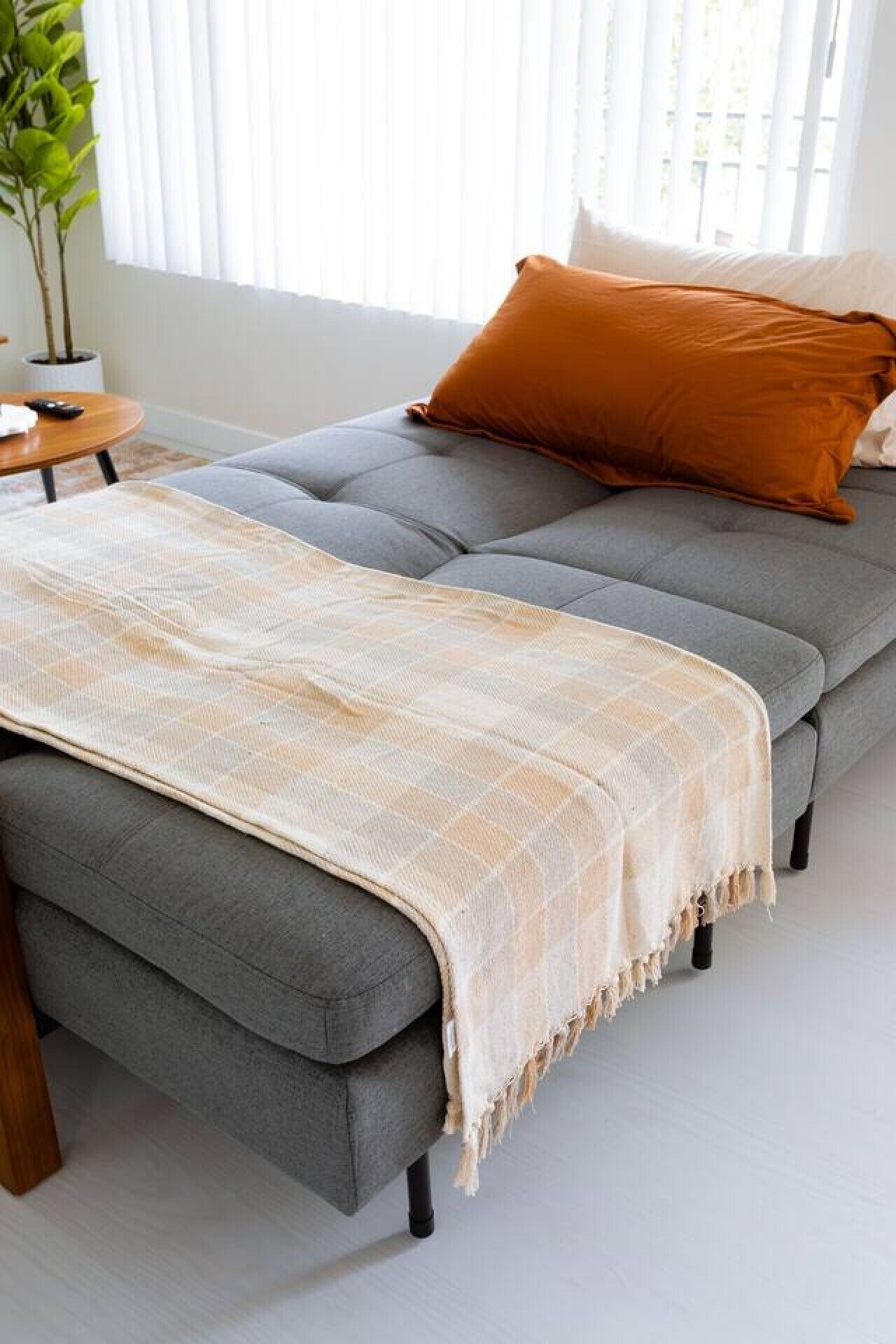 A grey sofa with a beige throw blanket and a single orange pillow.