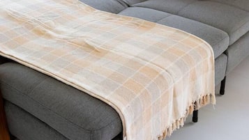 A grey sofa with a beige throw blanket and a single orange pillow.
