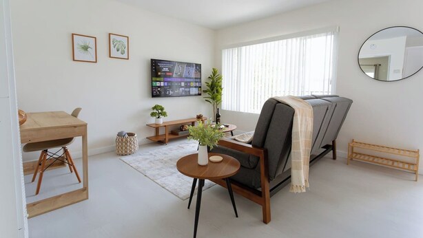 Ein Wohnzimmer mit einer Couch, einem an der Wand befestigten Fernseher, einem kleinen Holztisch und einem runden Couchtisch.