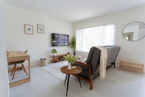 A living room with a sofa, a TV mounted on the wall, a small wooden table, and a round coffee table.