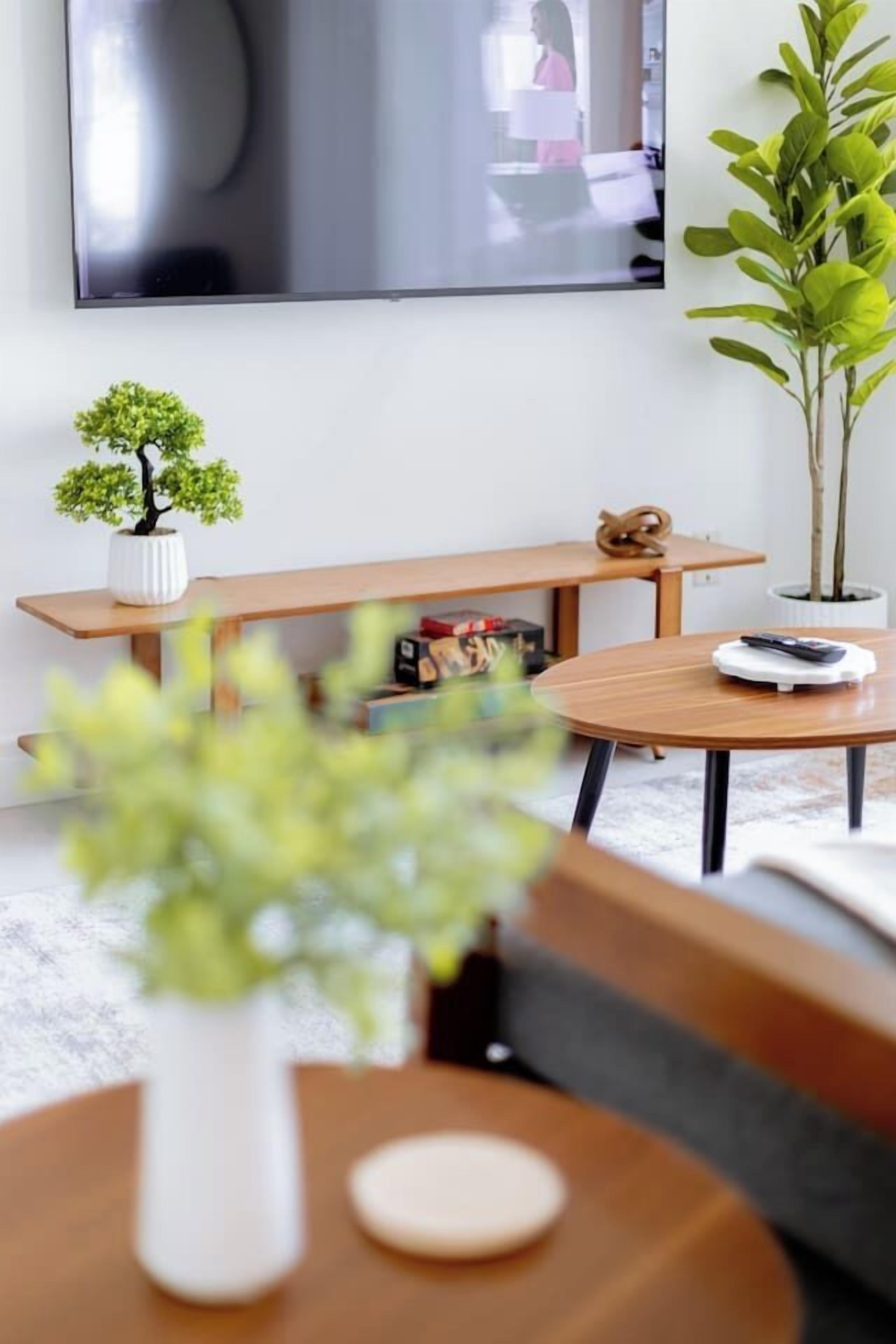 A modern living room with a round wooden table, a bench, a small potted plant, and a television mounted on the wall.