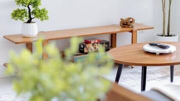 A modern living room with a round wooden table, a bench, a small potted plant, and a television mounted on the wall.