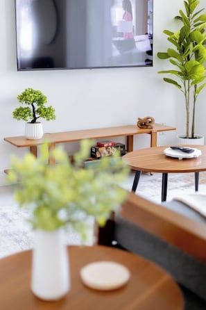 Una sala moderna con una mesa redonda de madera, un banco, una pequeña planta en maceta y un televisor montado en la pared.