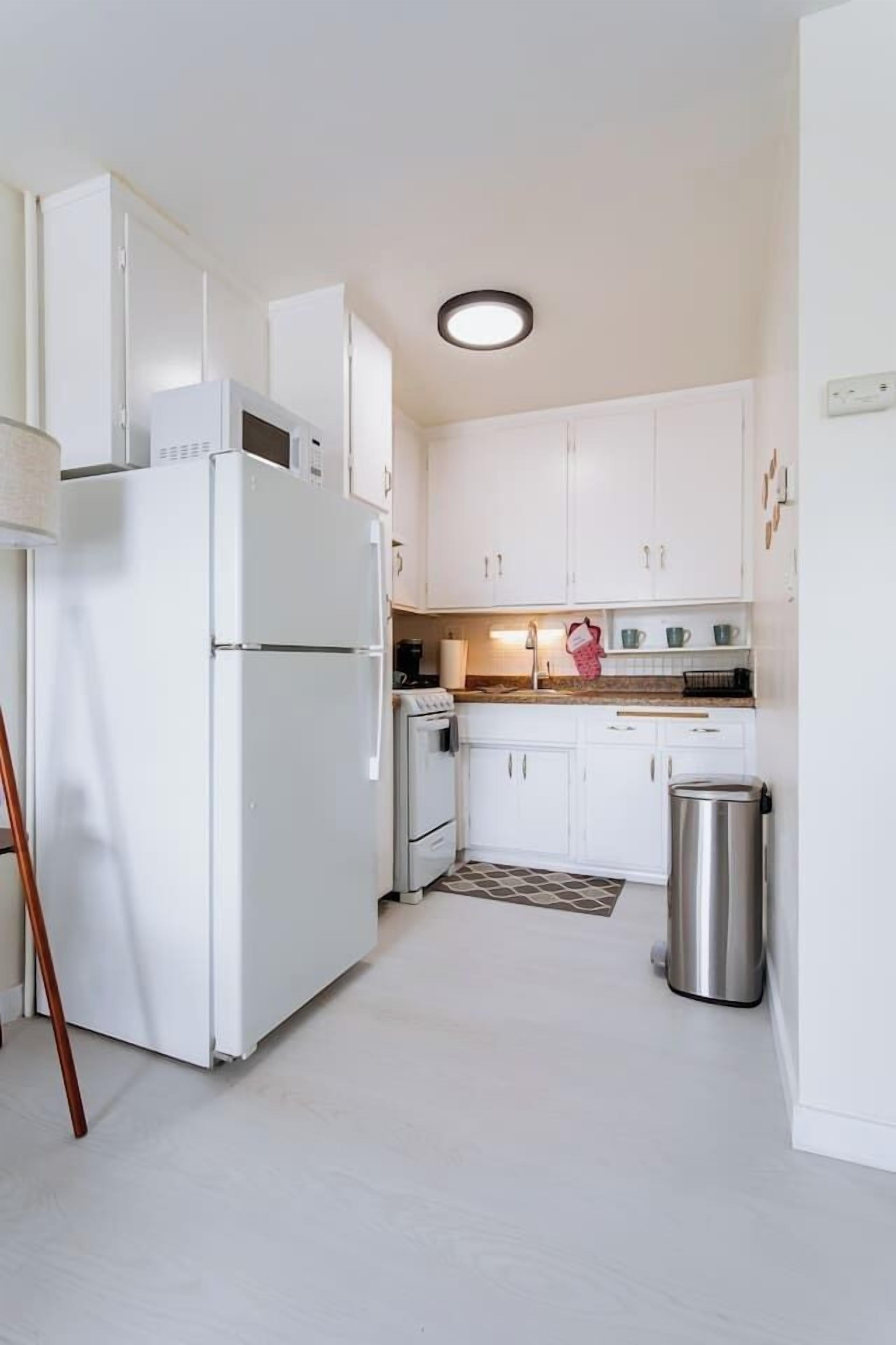 A compact kitchen with white cabinets, a stainless steel trash bin, and a built-in microwave.