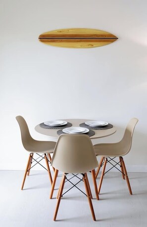 A dining area with a round table, four chairs, and a surfboard on the wall.