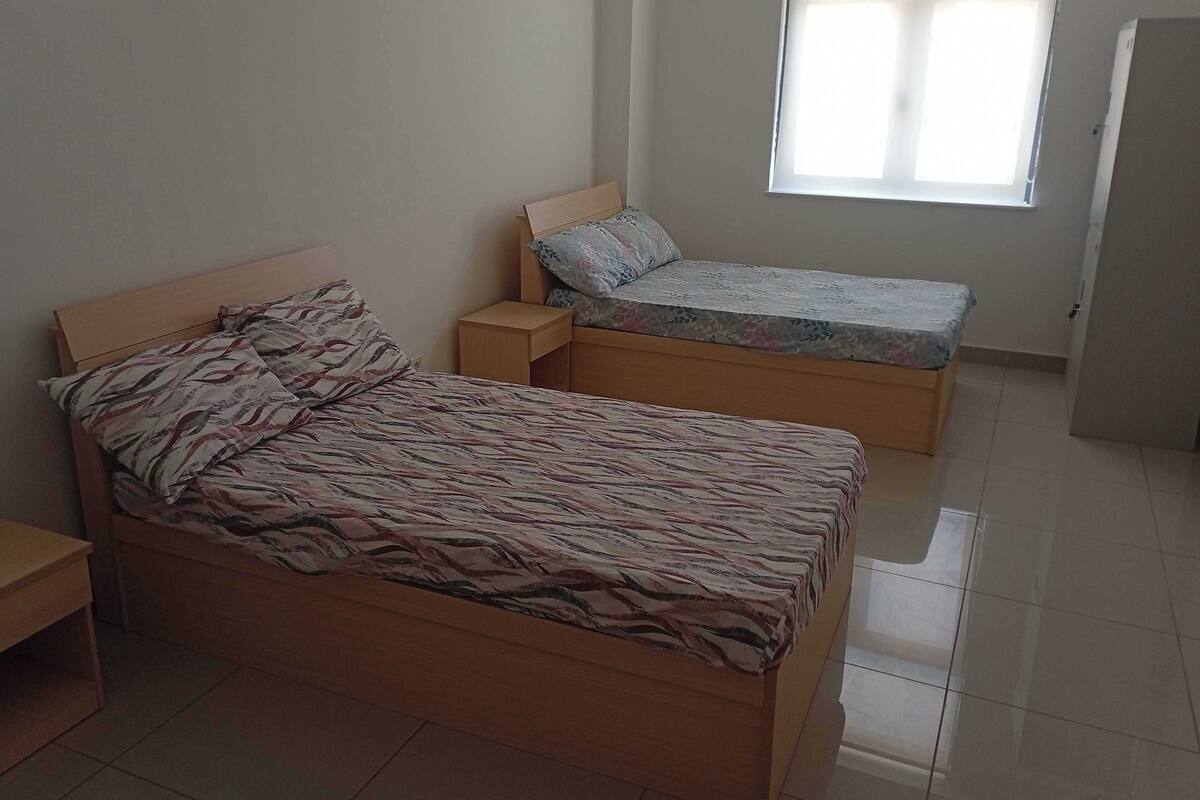 A bedroom with a large bed, a smaller bed, a nightstand, and a window.