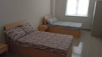 A bedroom with a large bed, a smaller bed, a nightstand, and a window.
