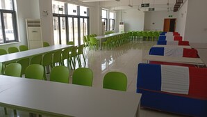 Ein geräumiger Essbereich mit langen Tischen und grünen Stühlen, großen Fenstern und einem klaren, modernen Design.