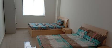 A bedroom with two beds, a window, and a door.