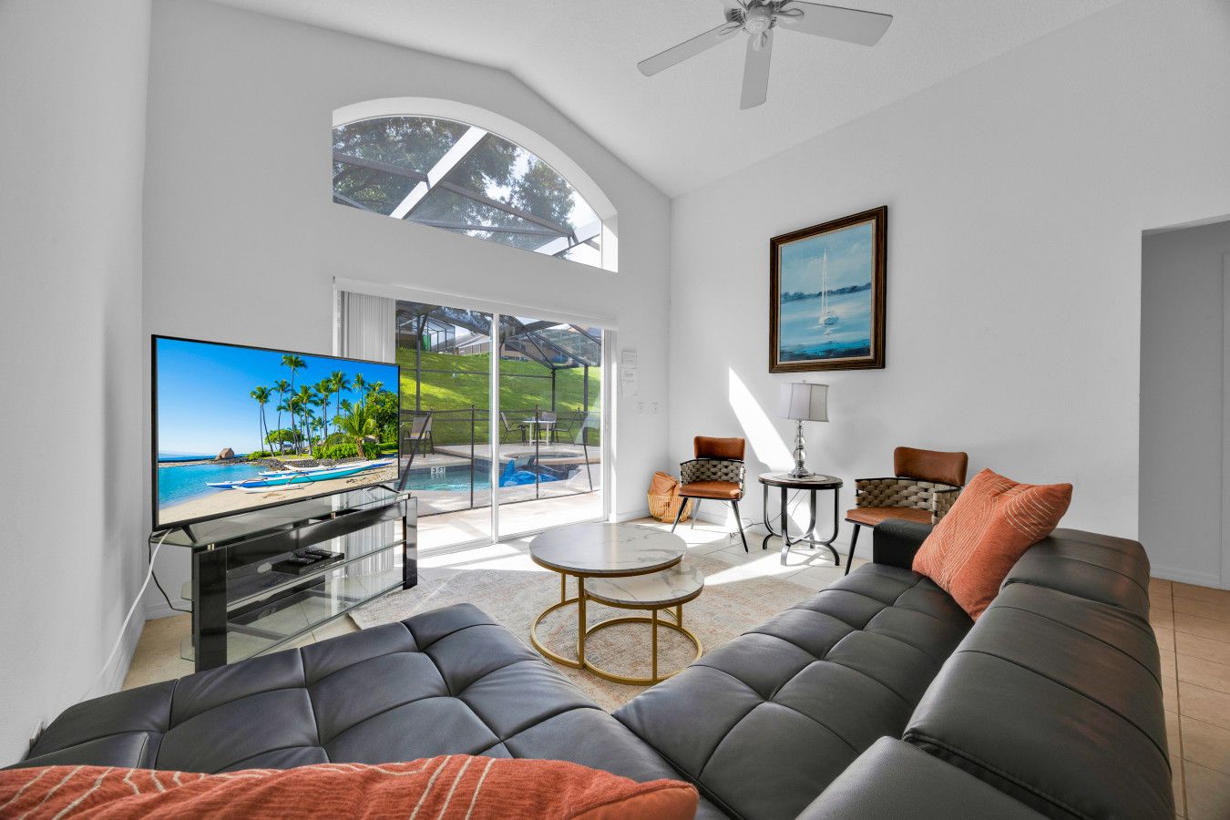 A modern living room with a large sectional sofa, a flat-screen TV, a round coffee table, and a view of a pool and outdoor area.