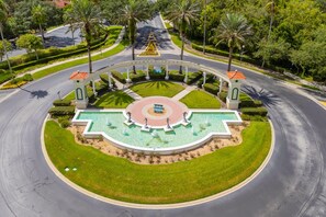A landscaped roundabout with a central fountain, surrounded by palm trees and well-maintained grass.