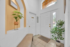 A hallway with a bench, a potted plant, and a door with a window above it.