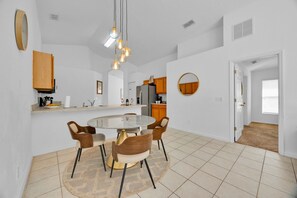 A modern kitchen with white cabinets, a central island, and a dining area with a round table and chairs.