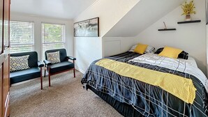 Un dormitorio con cama, dos sillas, un ventanal y una lámpara en el techo.