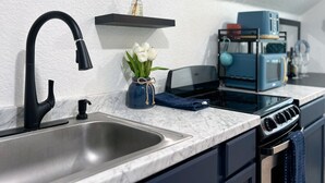 Una cocina moderna con un lavamanos de acero inoxidable, grifo negro y una cafetera azul.