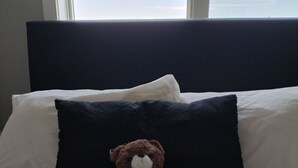 Ein Bett mit dunkelbraunem Kopfteil, weißen Kissen und einem braunen Teddybären auf einem weißen Kissen.