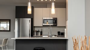 Une cuisine moderne équipée d’un réfrigérateur en acier inoxydable, d’un four à micro-ondes et d’un évier. Deux luminaires suspendus sont fixés au-dessus du plan de travail.