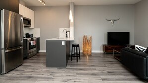 Une cuisine moderne avec un îlot central, un coin repas doté d’un canapé noir et un téléviseur à écran plat.