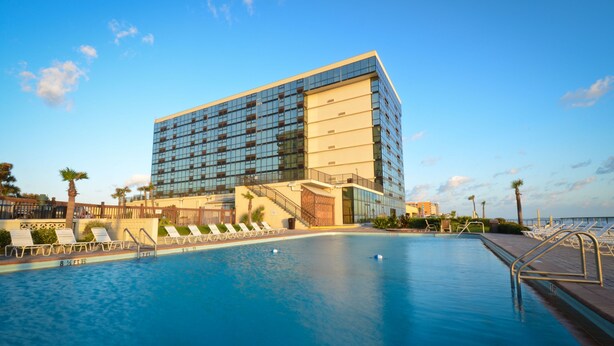 Un hôtel moderne doté d’une grande piscine, de chaises longues et offrant une vue dégagée sur l’océan.