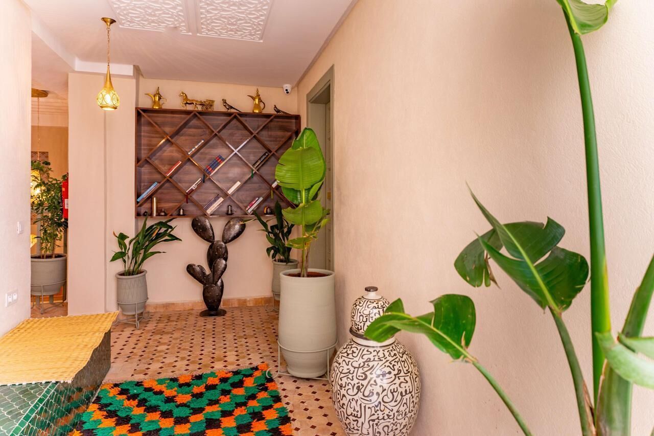 Un pasillo con piso estampado, plantas en macetas, un estante decorativo y un jarrón grande.