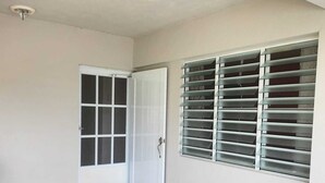 A room with a tiled floor, a white door with a window, and a wall-mounted air conditioning unit.