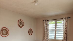 A living room with a brown sectional sofa, an ottoman, patterned wall decor, and a window with curtains.