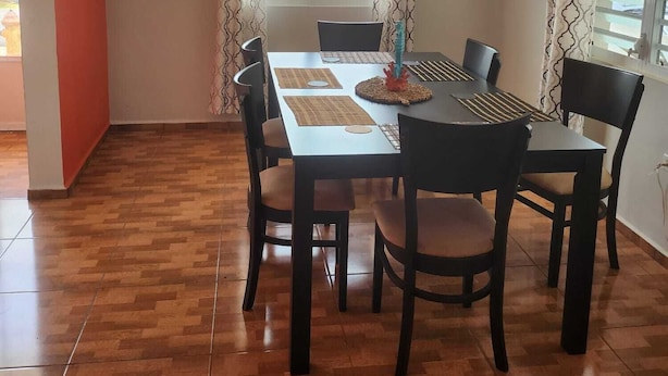 A dining area with a wooden floor, a table with chairs, and a window with curtains.