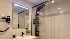 Un bagno moderno con doccia vetrata, un mobile lavabo bianco con specchio e un asciugacapelli fissato a parete.
