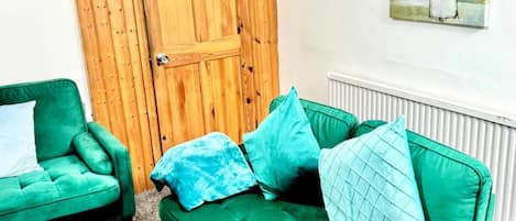 A room with a green sofa, a green armchair, and a wooden door.