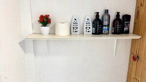 Estante con artículos de tocador, que incluye una planta en maceta, papel higiénico y diversos productos de cuidado personal.
