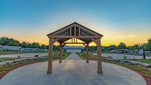 A covered pavilion with a concrete floor and a view of a parking area with RVs in the background.