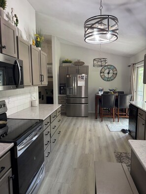 A modern kitchen with stainless steel appliances, a dining area with a table and chairs, and a large wall clock.