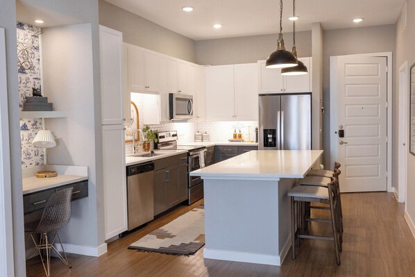 A modern kitchen with white cabinetry, stainless steel appliances, and a central island with bar stools.