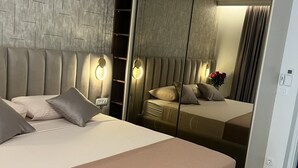 A modern hotel room with a large bed, a wardrobe with a mirror, and a wall with a geometric pattern.