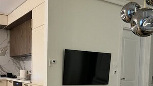 A modern kitchen with a built-in oven, a dining area with a round table, and a flat-screen TV mounted on the wall.