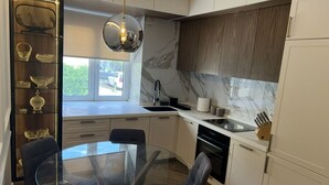 A modern kitchen with a glass dining table, white cabinets, and a marble backsplash.